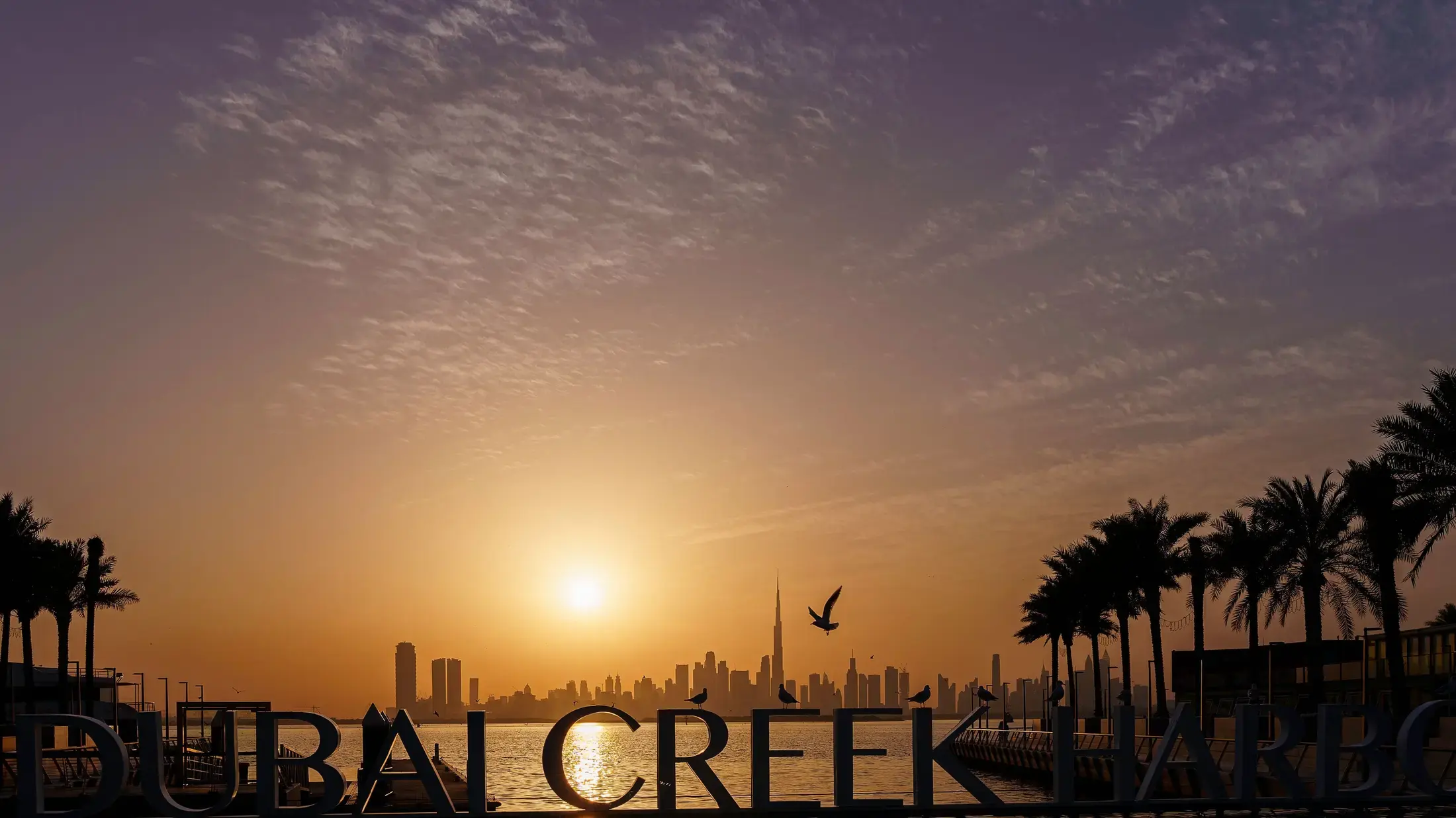 The Dubai Creek Harbour monument sign at sunset, the Downtown skyline across the water