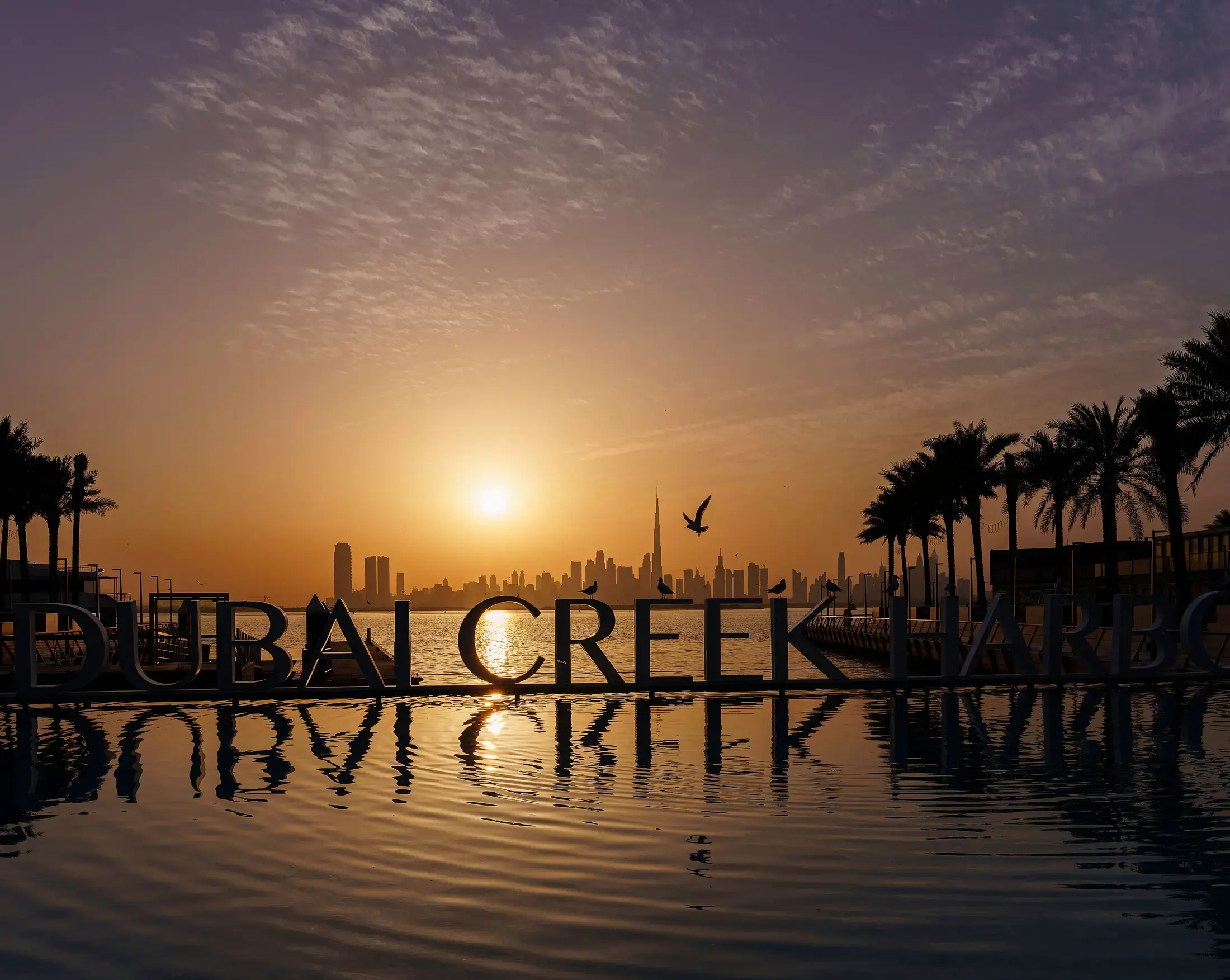 The Dubai Creek Harbour waterfront at sunset, the Downtown skyline beyond